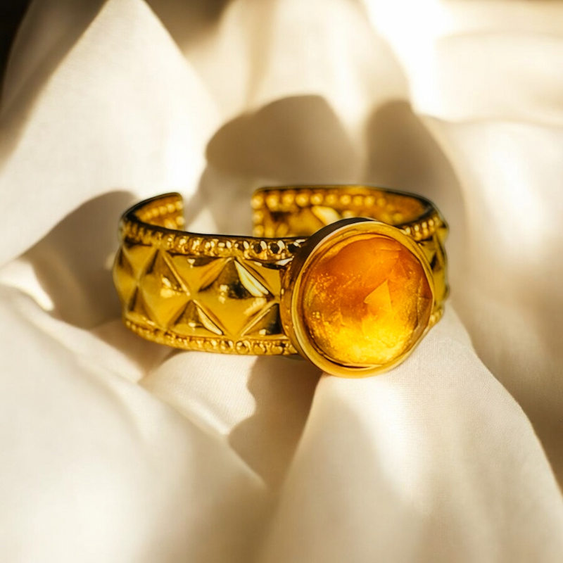 Un magnifique bracelet doré orné d'une pierre jaune, reposant sur un fond de tissu doux.