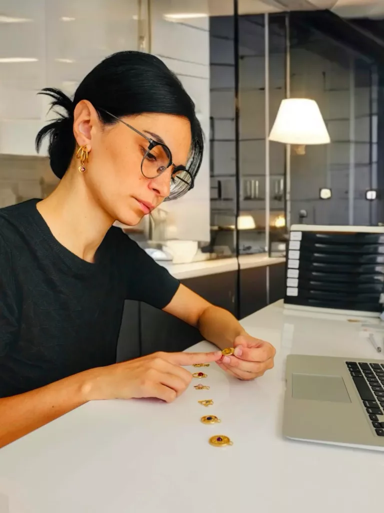 Créatrice de bijoux en plein travail, examinant des charms dorés avec précision dans un atelier moderne.